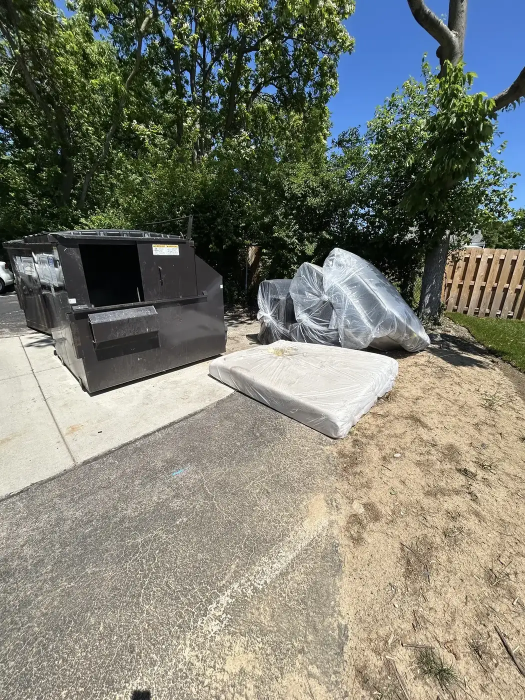 Phelps dumpster on a driveway with mattress and household debris loaded